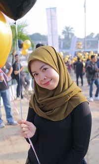 Portrait of smiling woman in hijab while standing on street in city