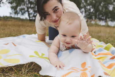 Playful mother and daughter having fun sitting on picnic blanket at park