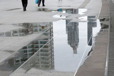 Low section of people walking on road by buildings in city