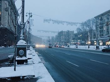 Cars on road by snow covered city against sky