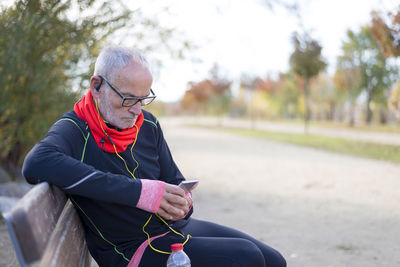 Senior man using smart phone while listening music on park bench