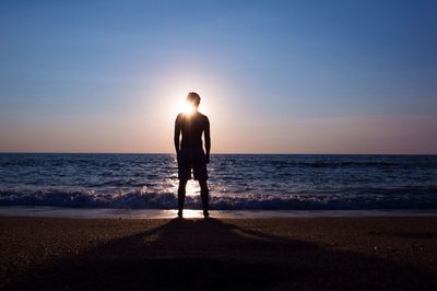 Silhouette person standing at seashore against sky during sunset