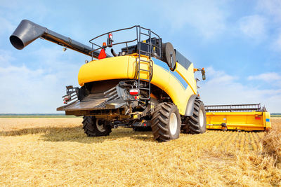 A large yellow agricultural harvester harvesting crops against the backdrop of a wheat field on day.