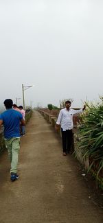 Rear view of men walking on footpath against clear sky