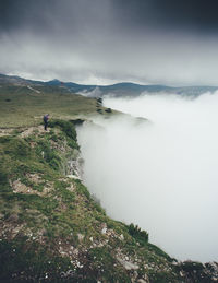 Mid distance view of woman standing on mountain against cloudy sky during foggy weather
