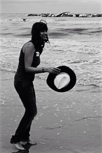 Side view of young woman holding sunglasses on beach