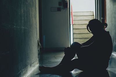 Side view of silhouette man sitting against building