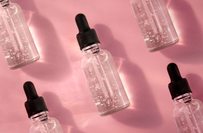 Pattern of transparent glass dropper bottle with serum on pink background. pipette with fluid acid