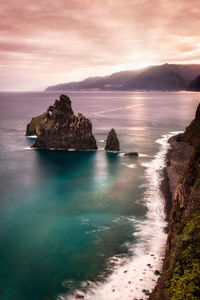 Rocks in sea against sky during sunset