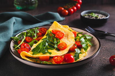 French omelette filled with cherry tomatoes and arugula on a plate on the table