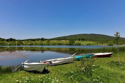 Boats moored in lake against clear blue sky