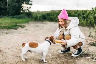 Happy teenage girl hugging and feeding her dog jack russell terrier in a field 