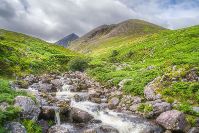 Scenic view of stream flowing amidst rocks against sky