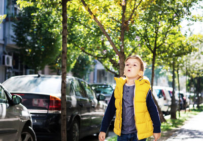 Boy standing by car against trees in city