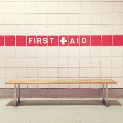 Empty bench against first aid text on wall