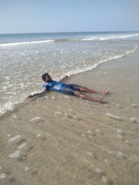 Young man lying on beach against clear sky