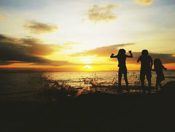 Silhouette people on beach against sky during sunset