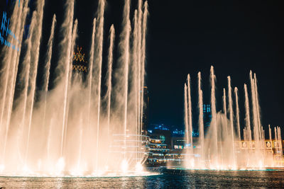 Digital composite image of illuminated fountain against sky at night