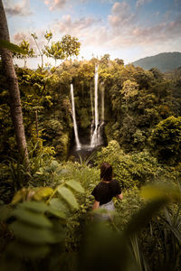 Rear view of man amidst waterfall against sky