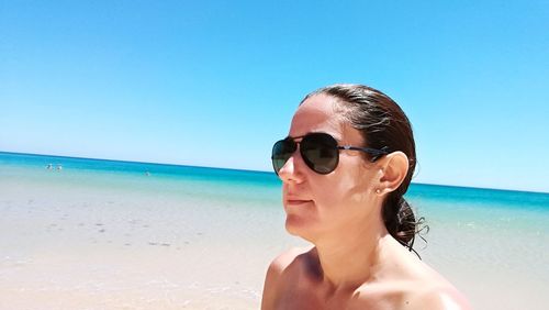 Young woman wearing sunglasses at beach against clear blue sky