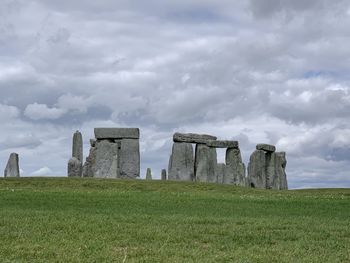 Stonehenge on field against cloudy sky