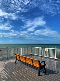 Empty bench by sea against sky