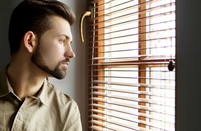 Close-up of thoughtful man looking through window at home