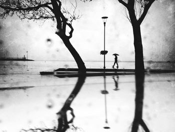 Silhouette man standing by tree with reflection in water