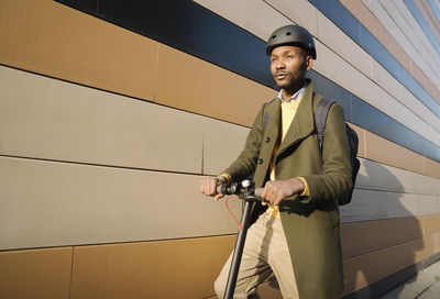 Stylish man with helmet and scooter at a building