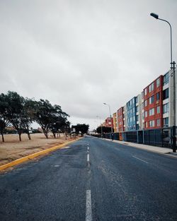 Empty road along trees and buildings