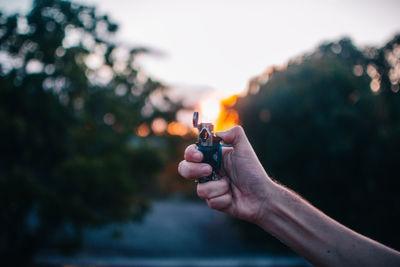 Close-up of hand holding illuminated light against sky during sunset