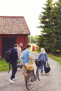 Friends with luggage and bicycle walking on road by cottage