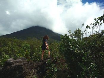 Full length of woman walking on rock in forest against sky