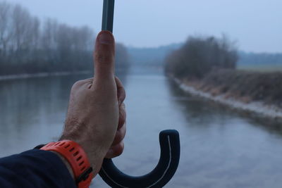 Close-up of man hand by lake against sky