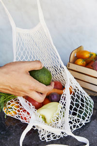 Man puts avocado to the eco string bag with fresh vegetables - tomatoes, purple potatoes, eggplants