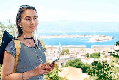 Tourist woman observes buildings near the panoramic view of messina, sicily, listening audio guide.