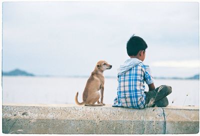 Rear view of boy sitting by dog