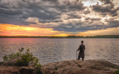 Rear view of man standing on shore against sky during sunset