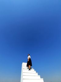 Low angle view of woman standing on steps against clear blue sky