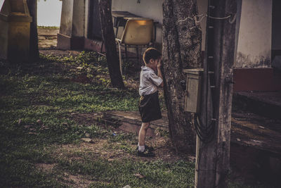 Boy playing hide and seek behind tree trunk