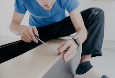 A man is repairing an old cabinet, tightening a screw with a screwdriver.