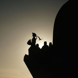 Low angle view of silhouette man holding camera against sky during sunset