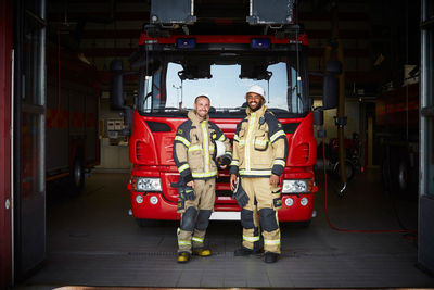 Portrait of firefighters standing in front of fire engine at fire station