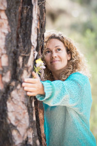 Portrait of young woman standing on tree trunk