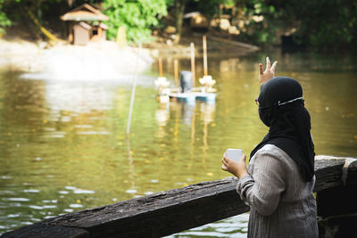 Hijab young girl feeding fish at the lake pond. view from behind.