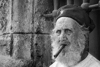 Old man with a beard and his beret smokes a cigar on a street in old havana