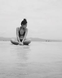 Young woman sitting at sea shore against sky