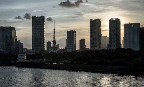 Modern buildings by river against sky in city