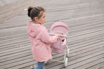 Young girl playing with her toy stroller on the boardwalk