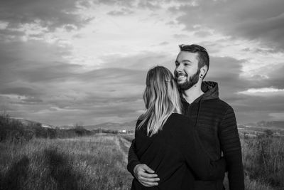 Couple embracing while standing on field against sky